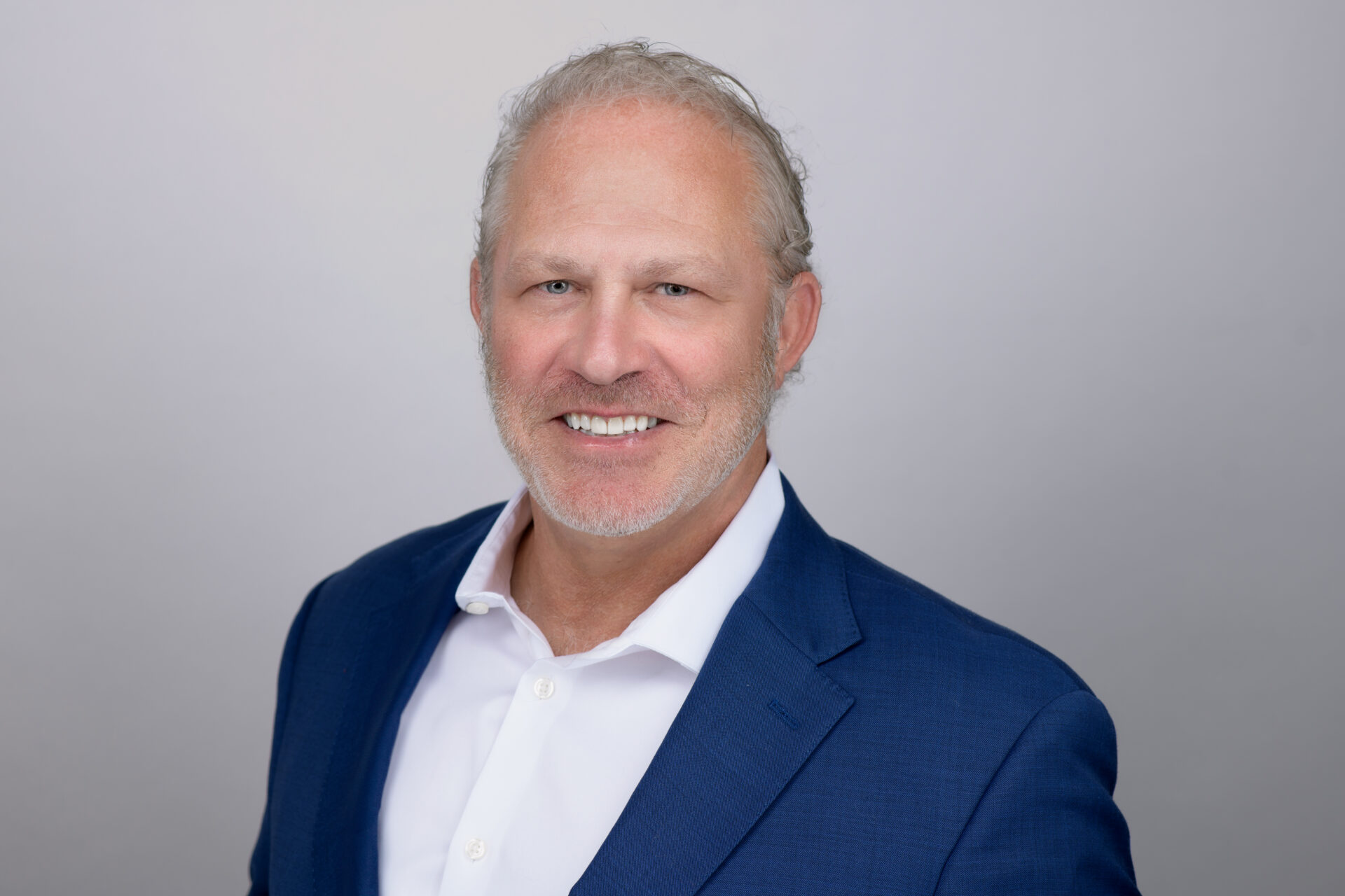 Professional headshot of a smiling man with graying hair wearing a blue blazer and white shirt.