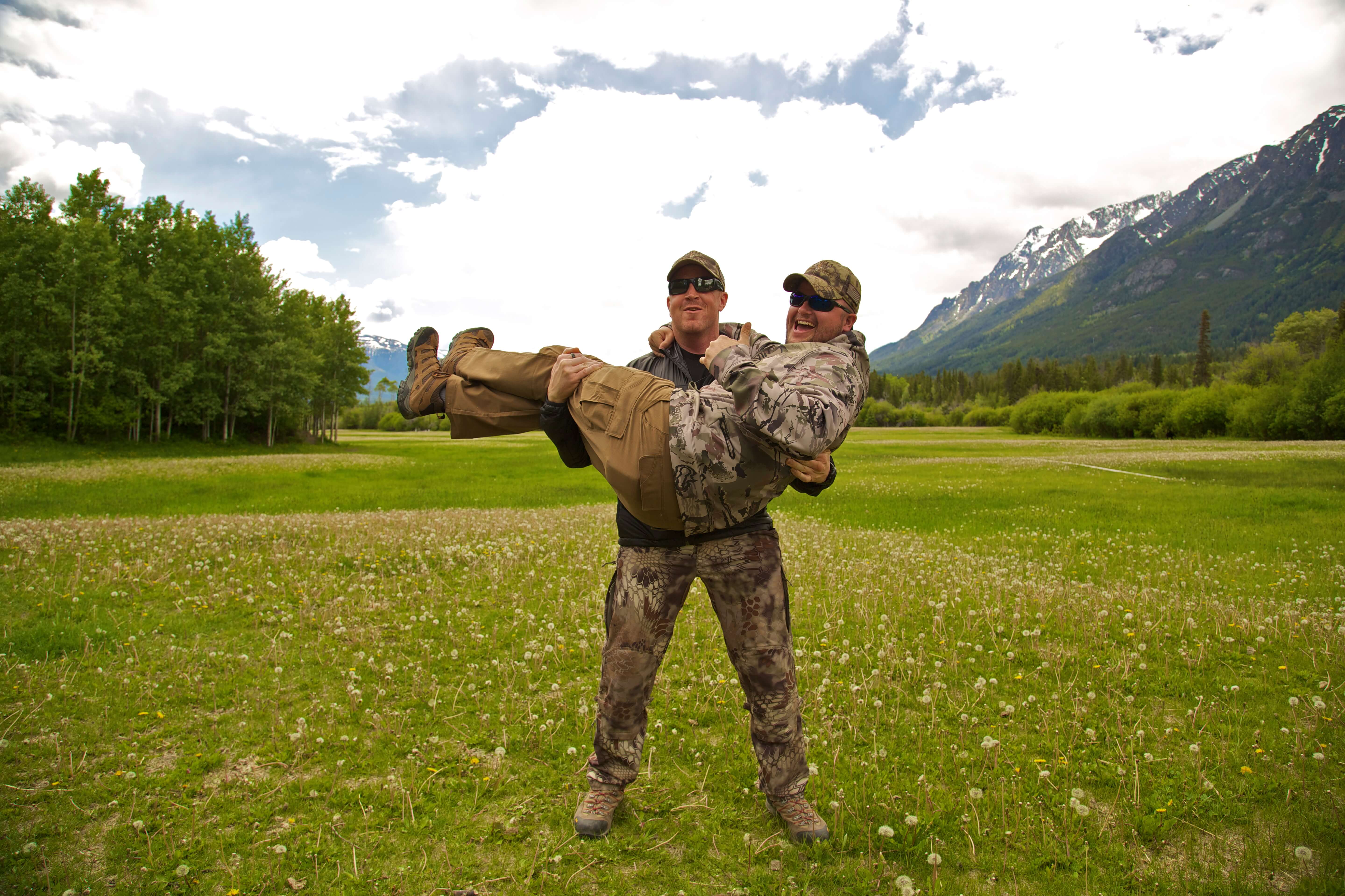 Two men in camouflage holding each other in a field