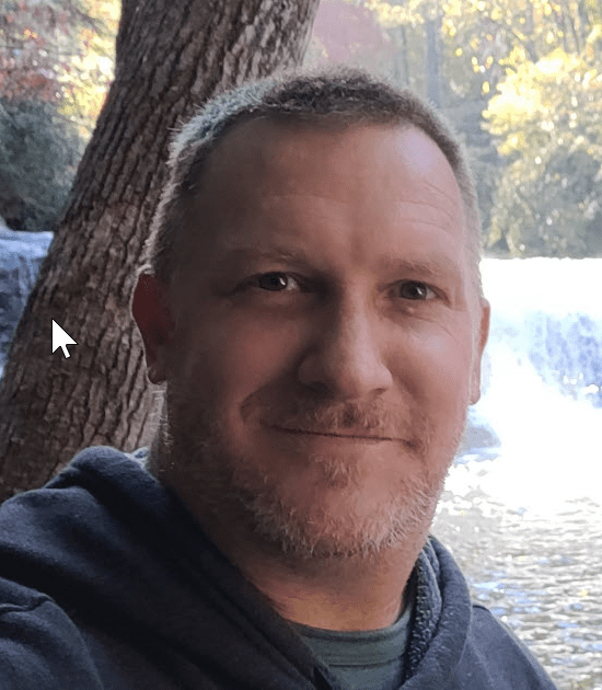 Man with a slight smile posing in front of a waterfall.