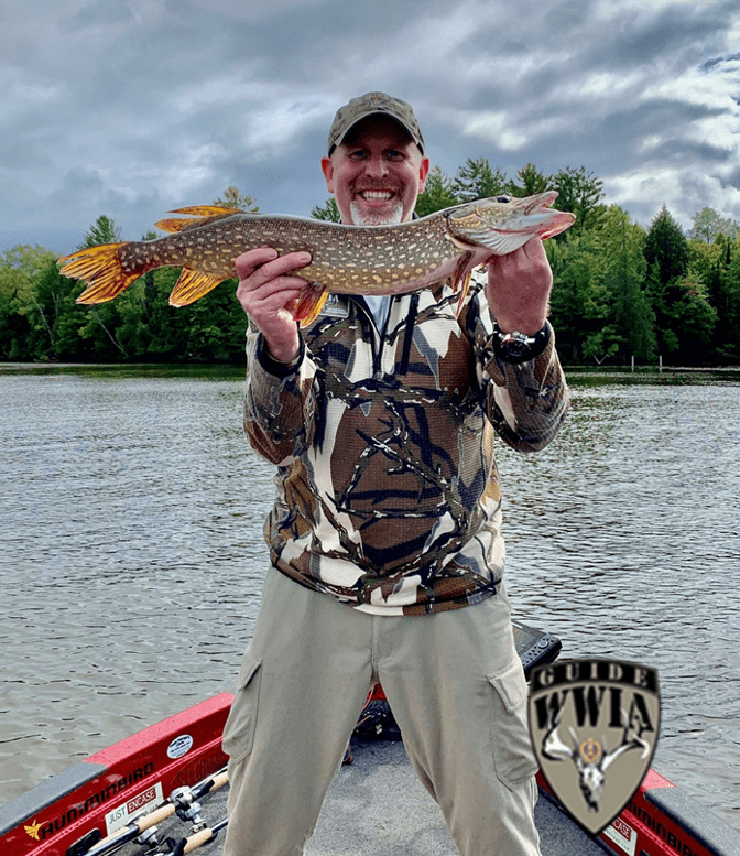 A man holding up a pike fish on a boat.