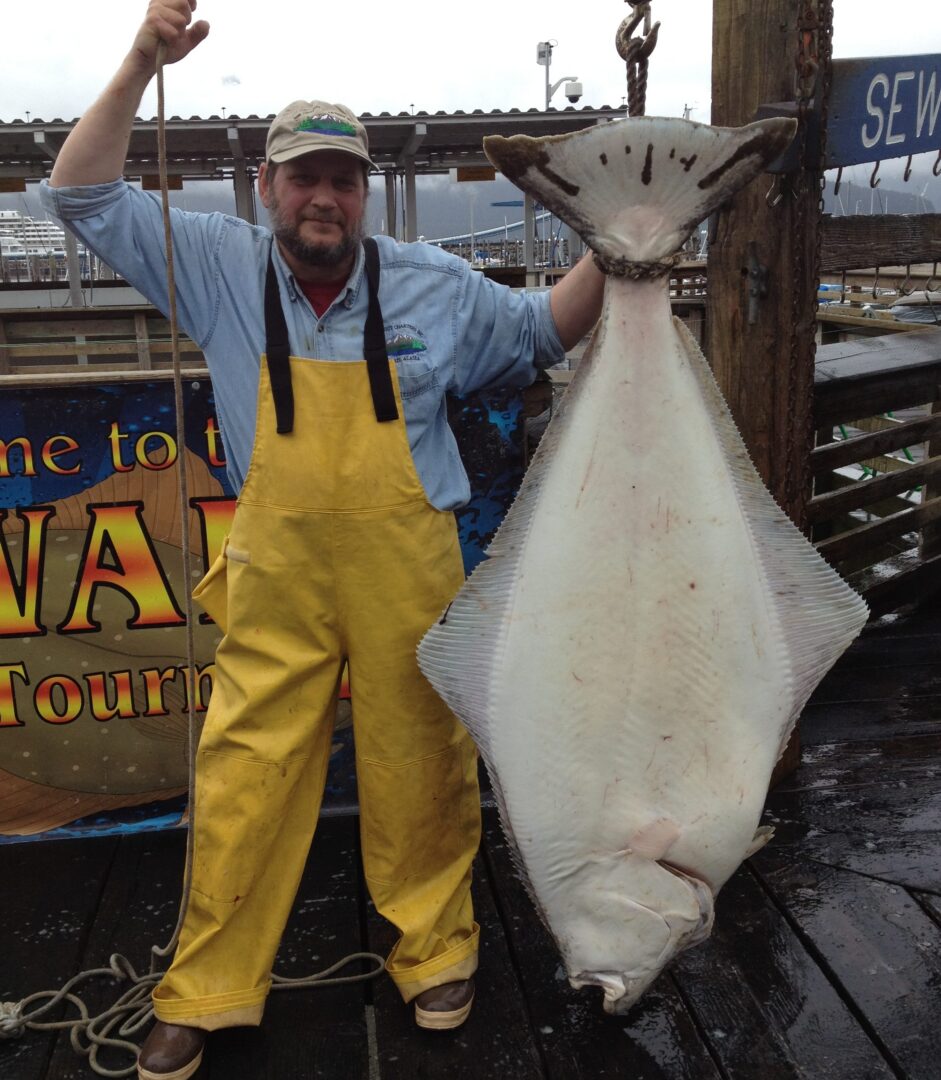 A man holding a large halibut on a dock.