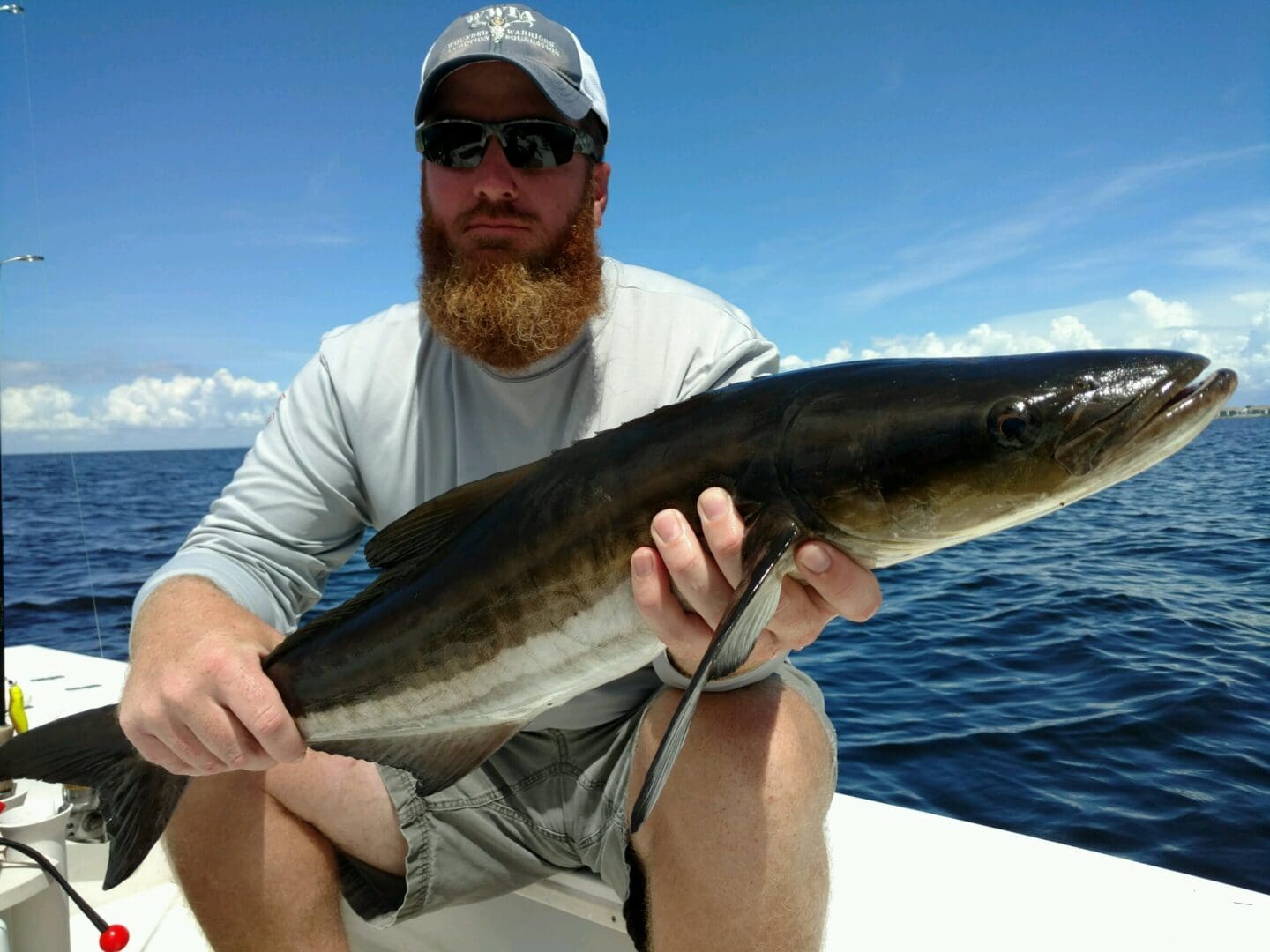 A man with a beard holding a fish on a boat