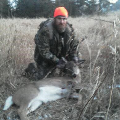 A man kneeling down next to a deer in a field.