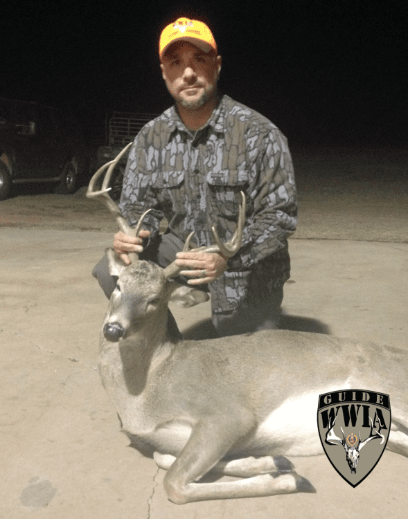 A man kneeling down next to a deer.