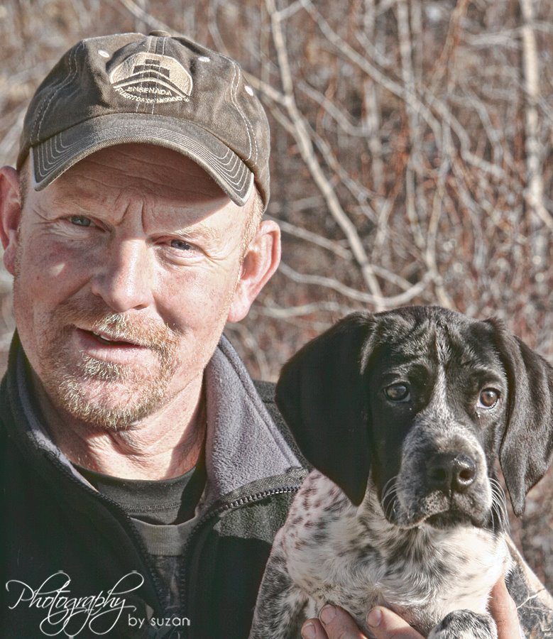 A man in a hat holding a black and white dog.