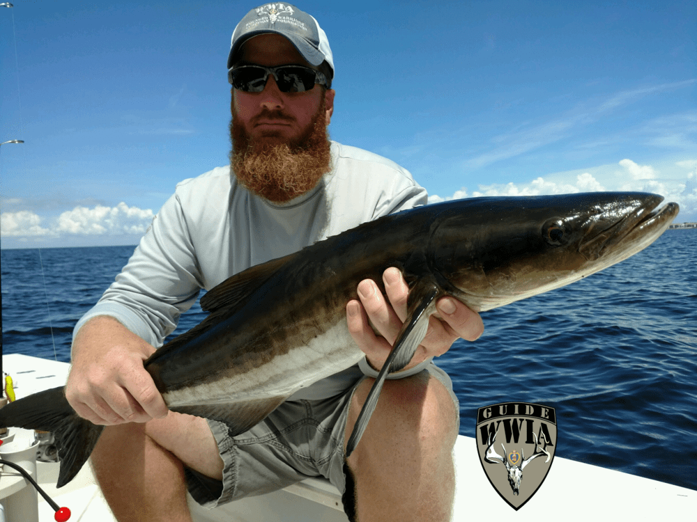 A man with a beard holding a fish on a boat.