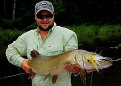 A man holding a large pike in the water.