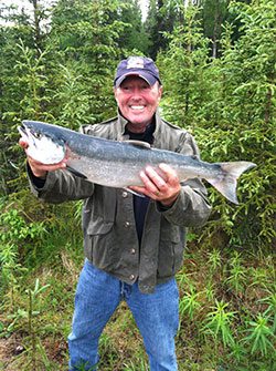 A man holding up a fish in the woods.