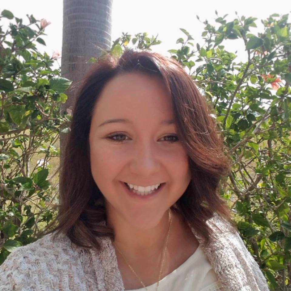 A woman smiling in front of bushes.