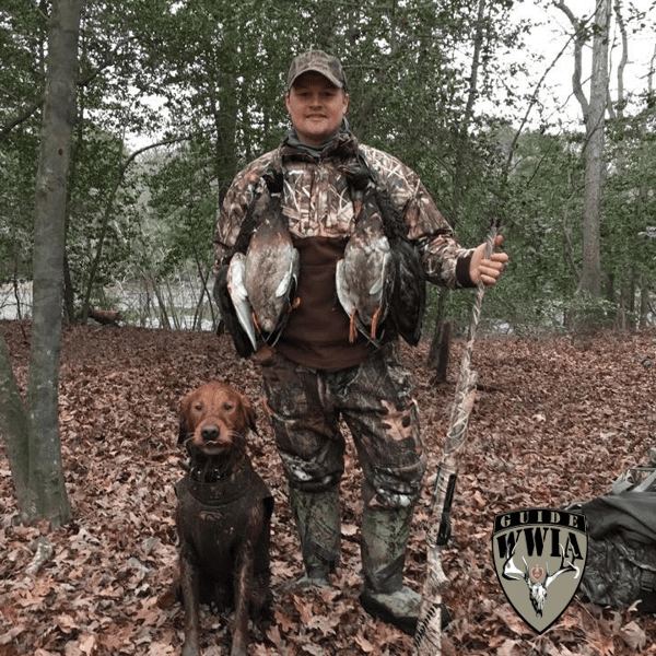 A man in camouflage with a dog and ducks.