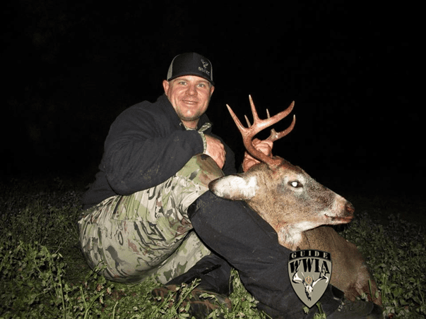 A man kneeling down next to a deer with antlers.