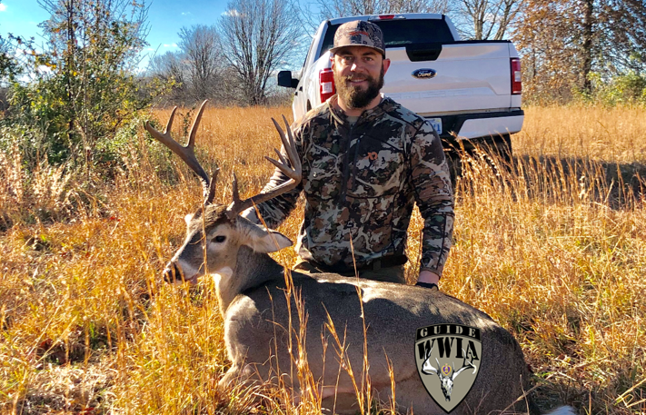 A man posing with a deer in a field.