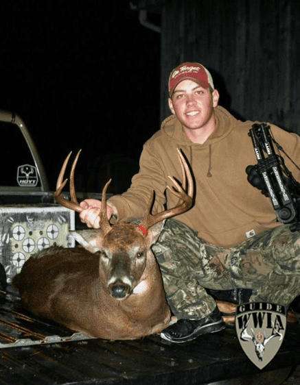 A man in camouflage kneeling next to a deer.