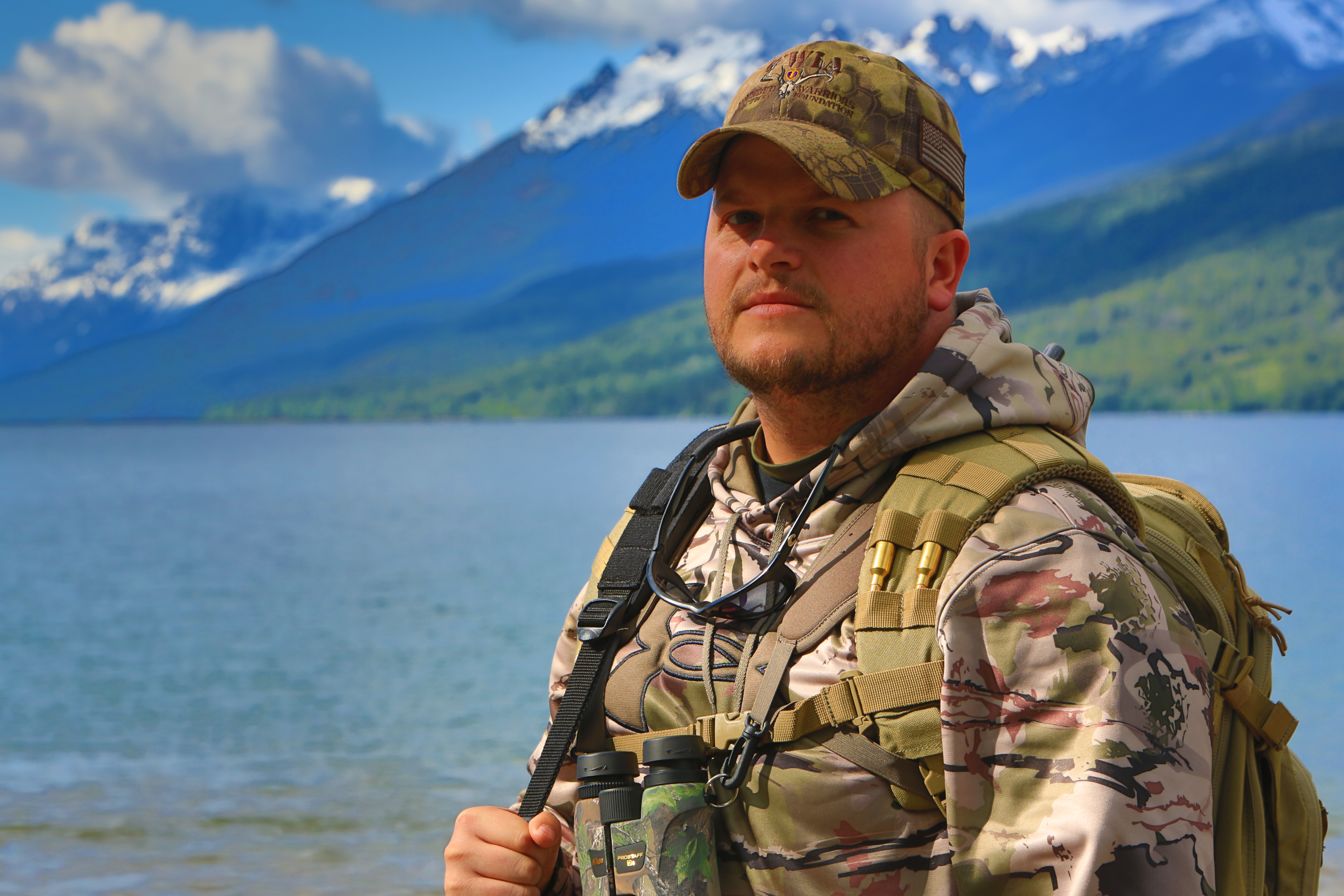 A man in camouflage standing next to a body of water.