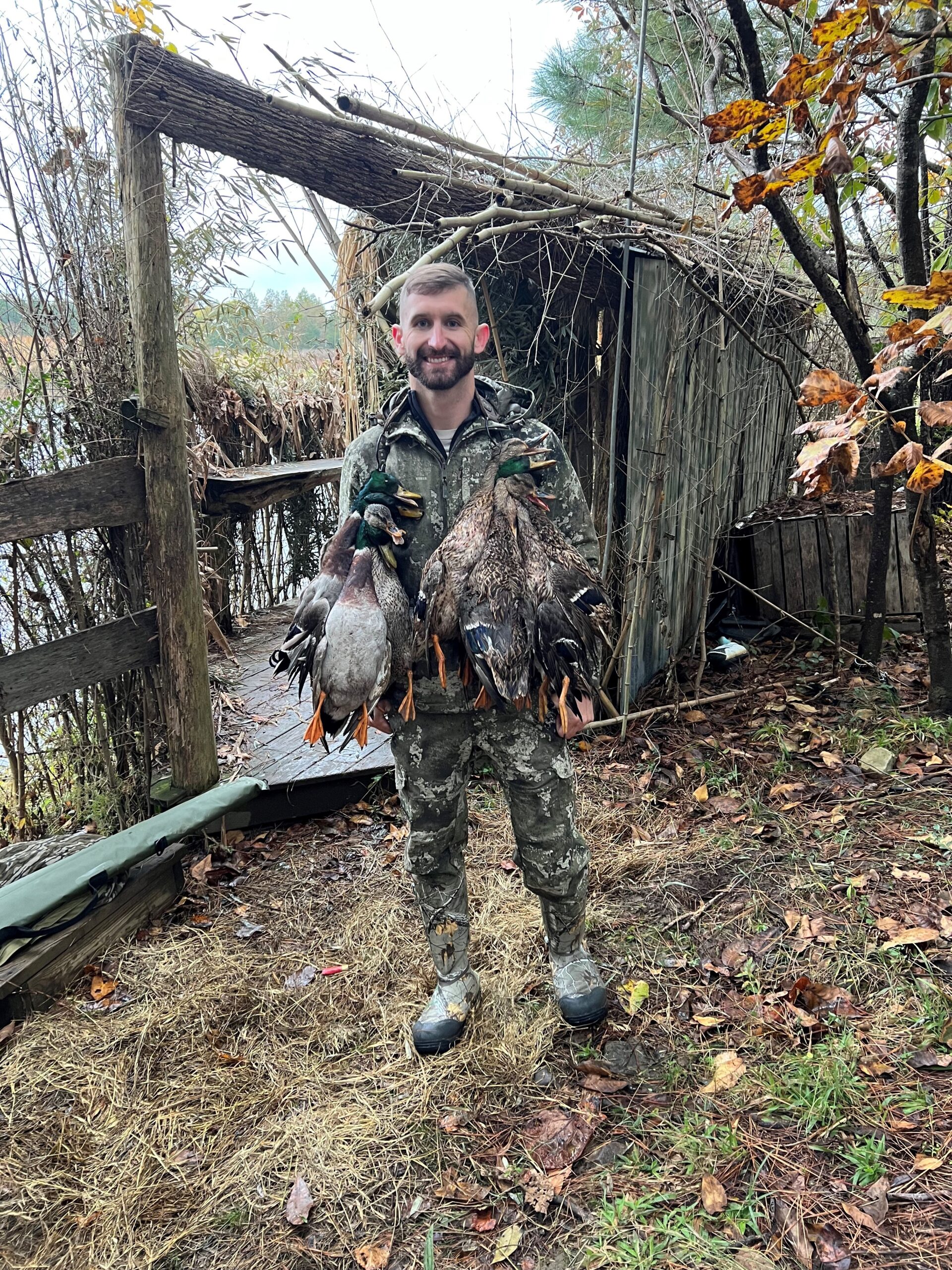 A man holding two ducks in front of a shed.