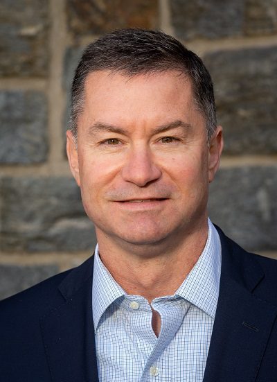 A man in a suit and tie standing in front of a stone wall