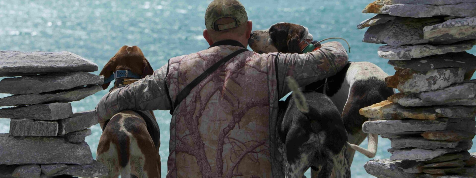 man hugging dogs with sea