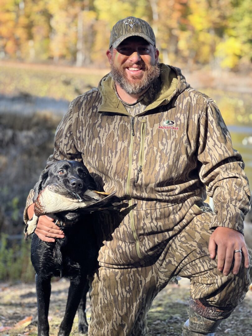 A man in camouflage with a dog and a duck.