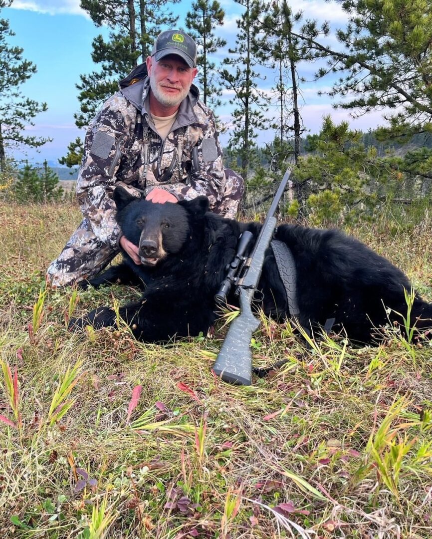 A man kneeling next to a black bear with a rifle.