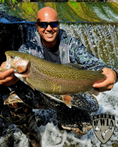 Man holding large rainbow trout by waterfall.