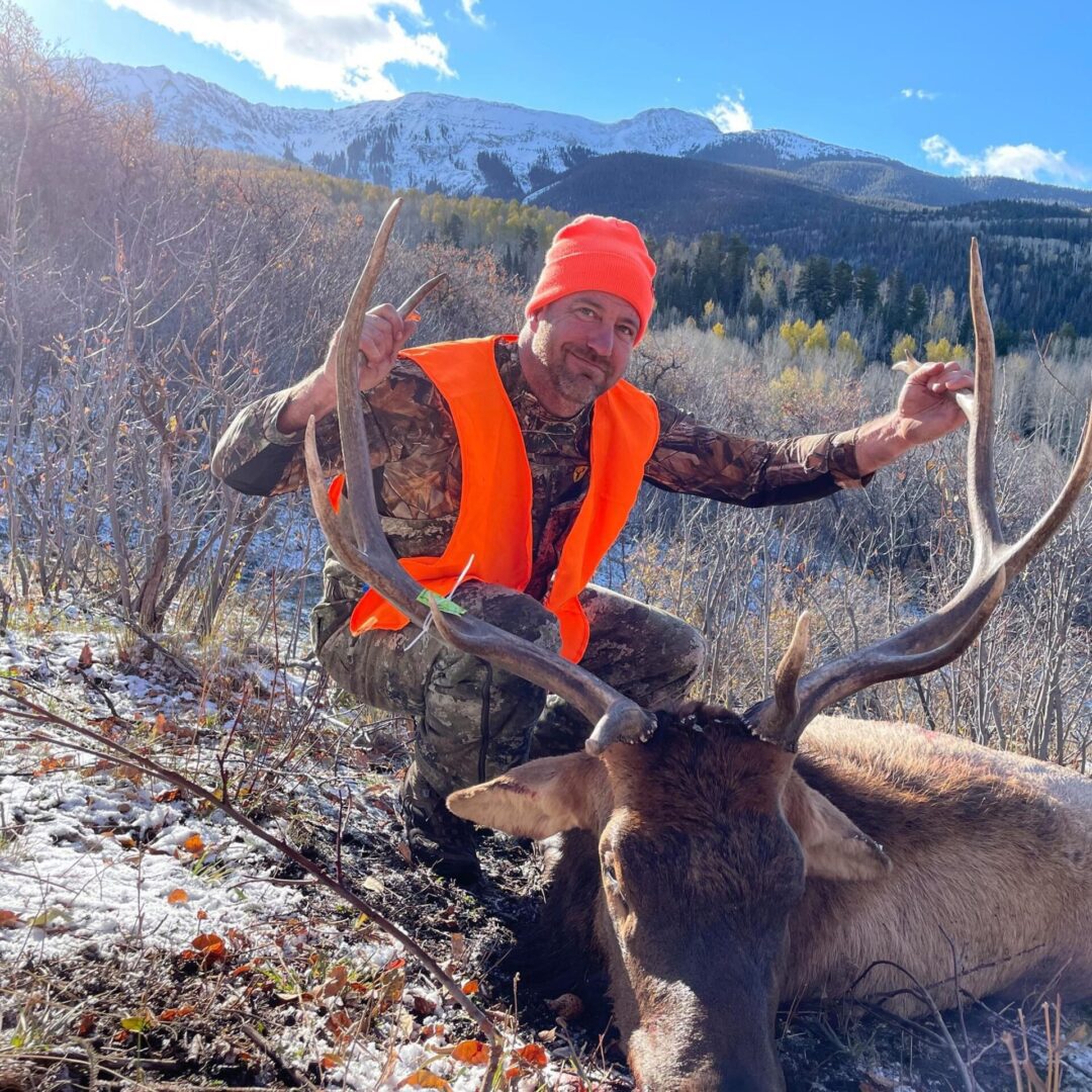 Hunter posing with an elk in snowy mountainous terrain.