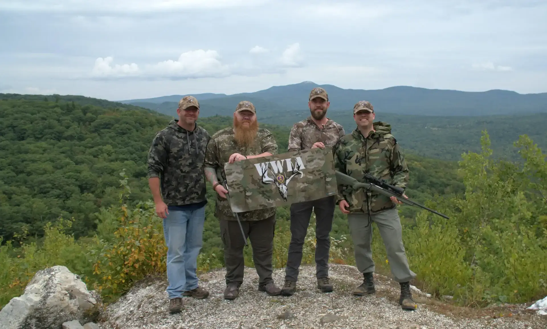Four men outdoors holding a KWIA flag