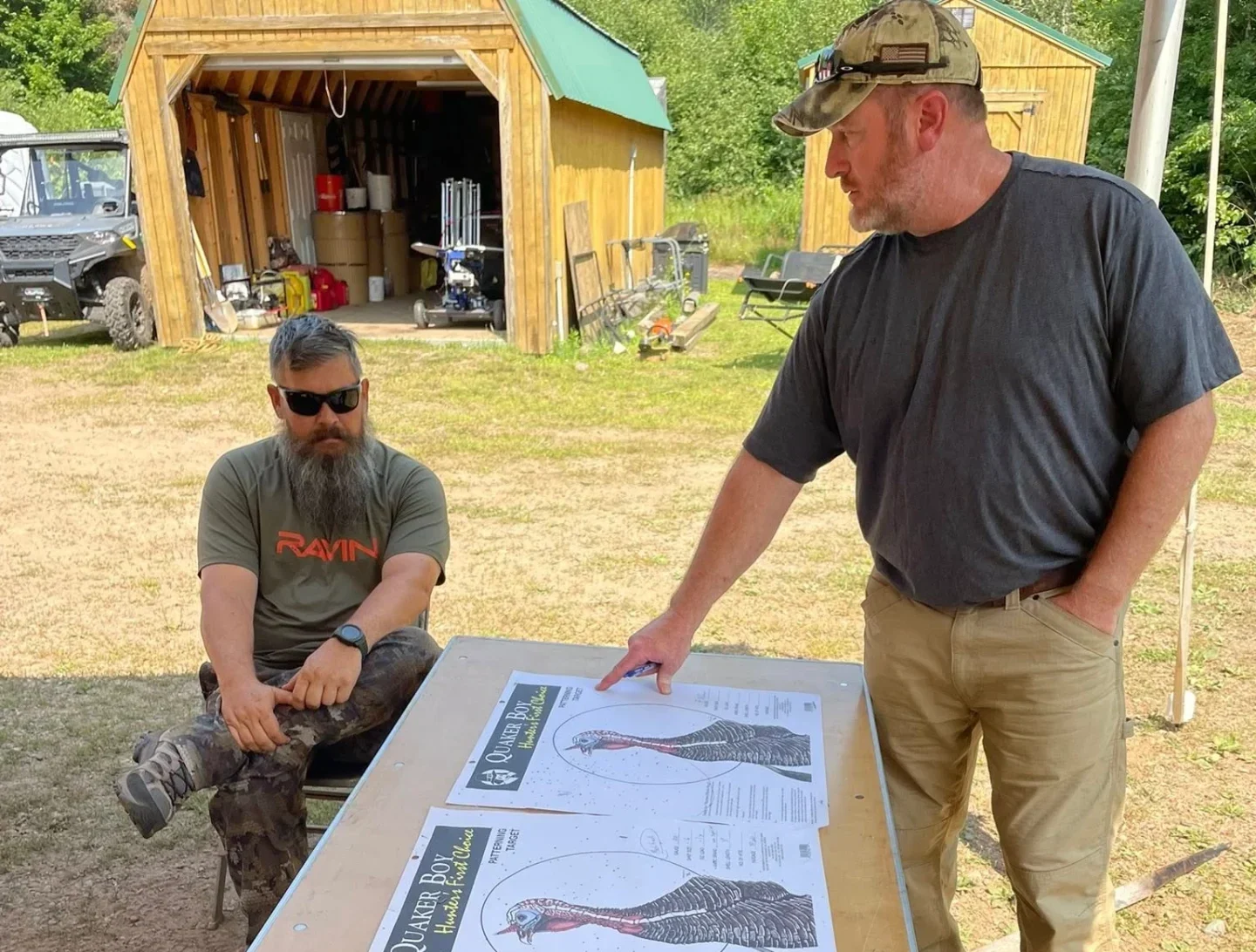 Two men discussing maps outside wooden shed