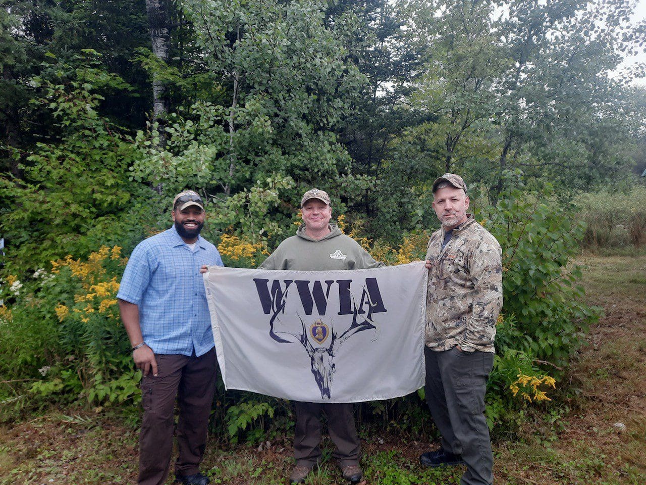Three men holding WWIA flag outdoors
